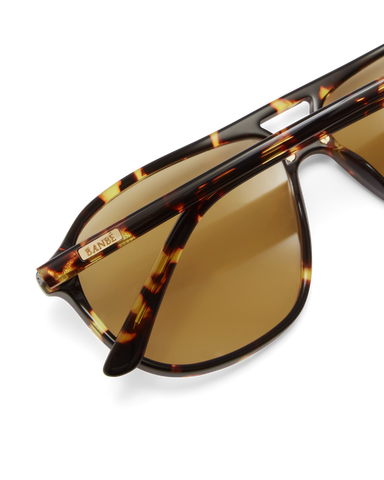 Women's aviator sunglasses in amber tort colourway featuring an oversized modified aviator silhouette with flat-top brow bar, double bridge, angular navigator-inspired shaping, and slim arms for a bold, contemporary look with full coverage.