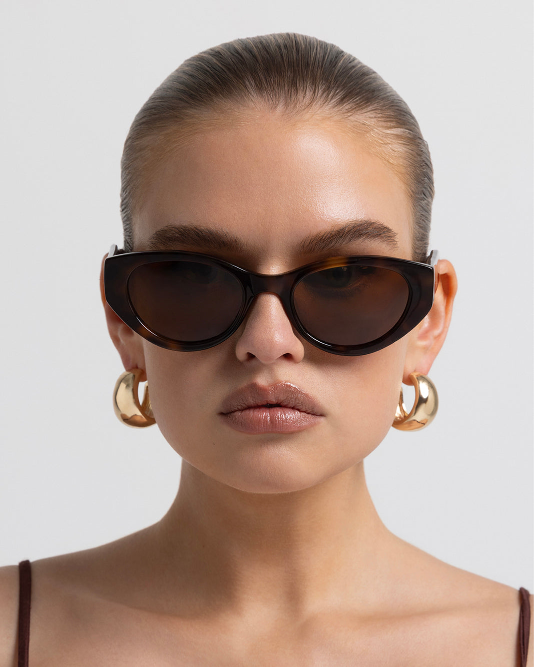 Model wearing women's sunglasses with thick sculpted brown cat-eye frames with a bold statement silhouette