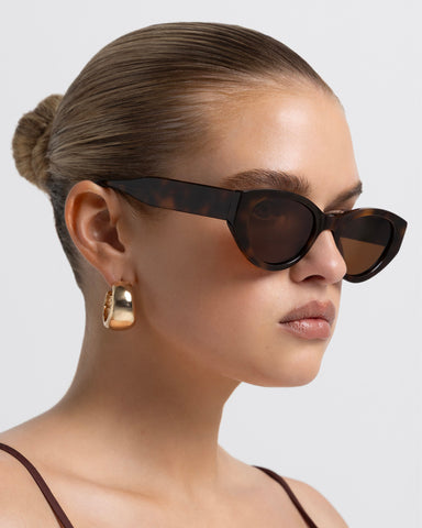 Model wearing women's sunglasses with thick sculpted brown cat-eye frames with a bold statement silhouette