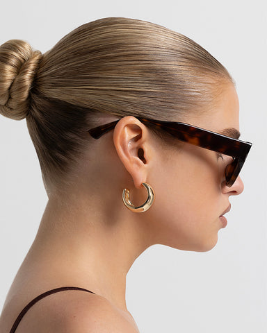 Model wearing women's sunglasses with thick sculpted brown cat-eye frames with a bold statement silhouette
