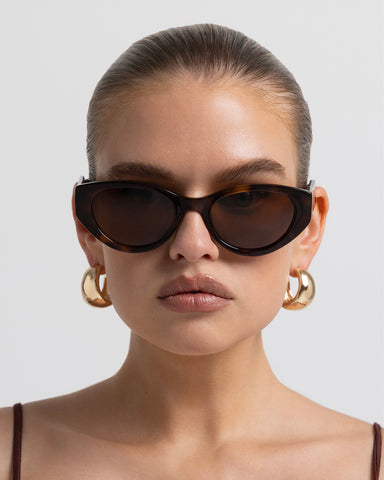 Model wearing women's sunglasses with thick sculpted brown cat-eye frames with a bold statement silhouette